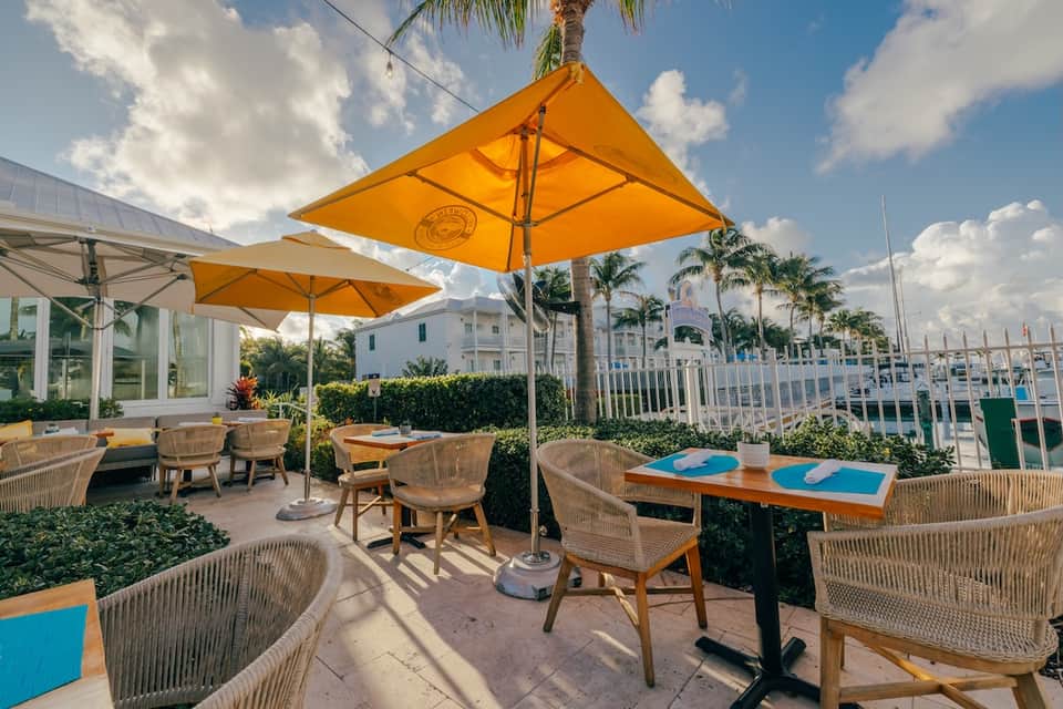 Waterfront terrace with golden umbrellas, woven chairs, marina view, and yacht docking facilities visible