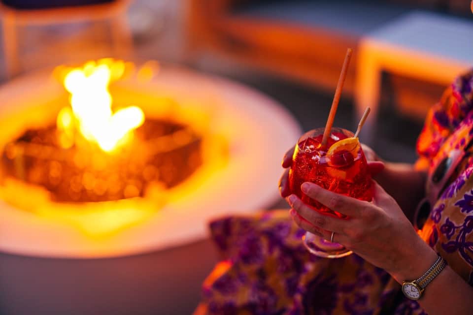 Person holding colorful cocktail with heart-shaped fire element during evening celebration