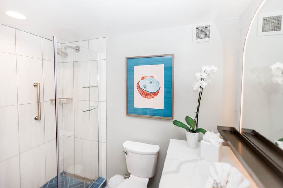 Modern bathroom with walk-in shower, white tile, and seashell artwork on blue frame