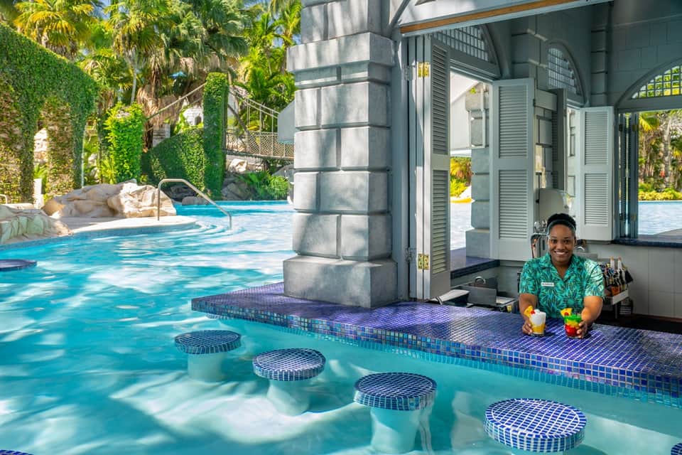 Poolside service station with attendant offering drinks near turquoise water and cabanas