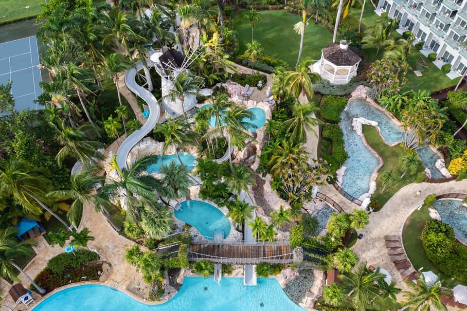 Aerial view of resort with multiple pools, winding waterslide, palm trees, and landscaped grounds