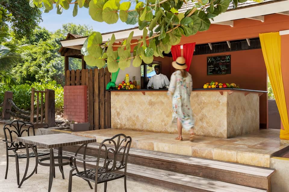 Outdoor tiki bar with orange awning, palm trees, and colorful arrangements on serving counter