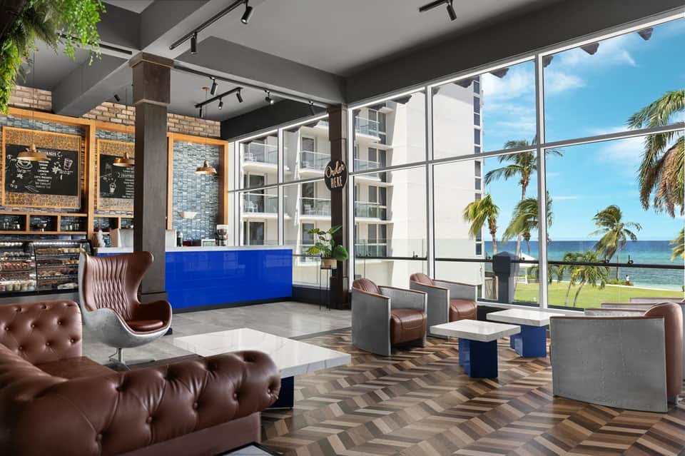 Contemporary hotel lobby with floor-to-ceiling windows overlooking beach, blue accent counter, and leather seating