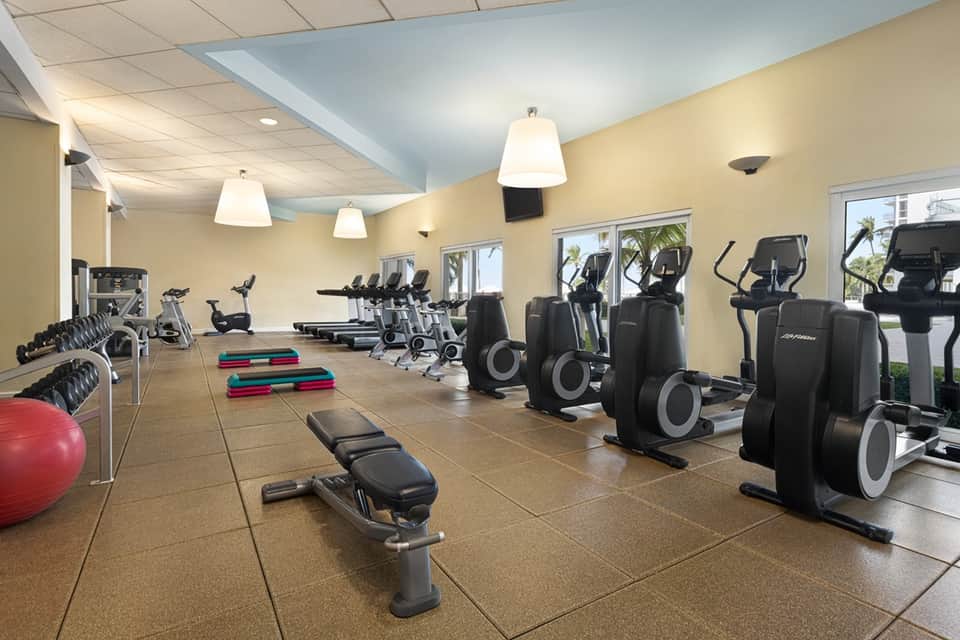 Bright fitness center with cardio equipment, weights, exercise ball, and large windows