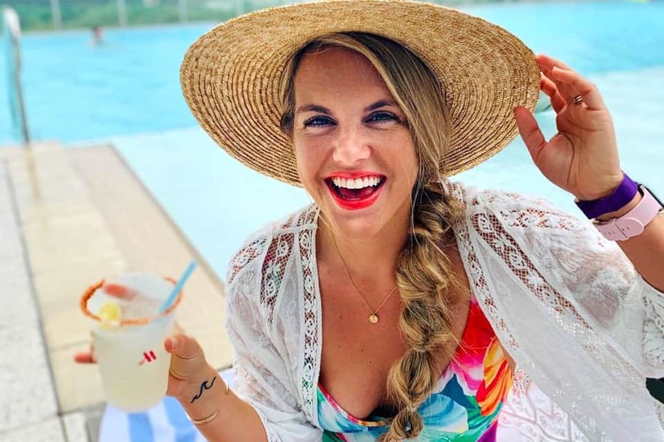 Woman in straw hat holding tropical drink by resort pool with colorful swimwear
