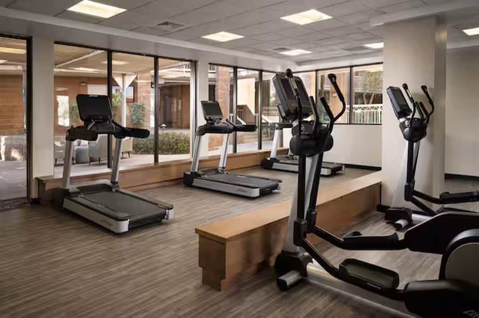 Fitness center with treadmills, elliptical machines, and large windows overlooking courtyard