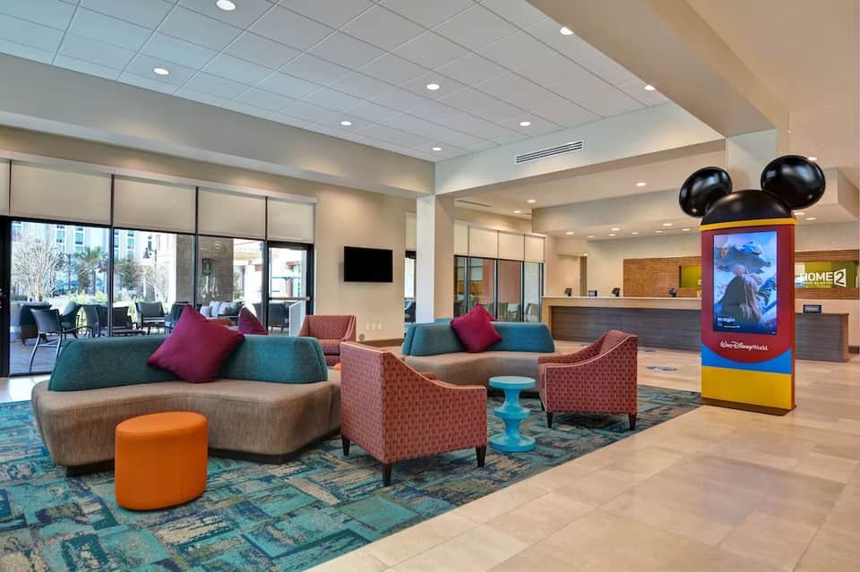Hotel lobby interior with colorful modern sofa, burgundy chairs, and Mickey Mouse display kiosk