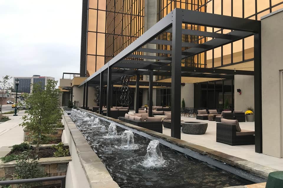 Contemporary outdoor patio with black pergola, lounge seating, water features, and tall buildings