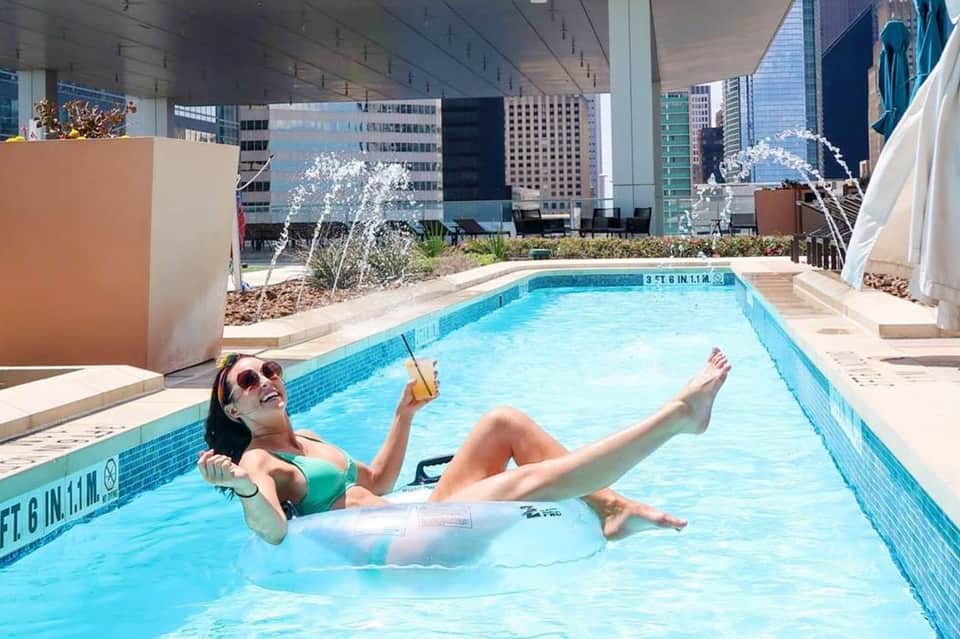 Woman relaxing on inflatable raft in rooftop pool with city skyline views