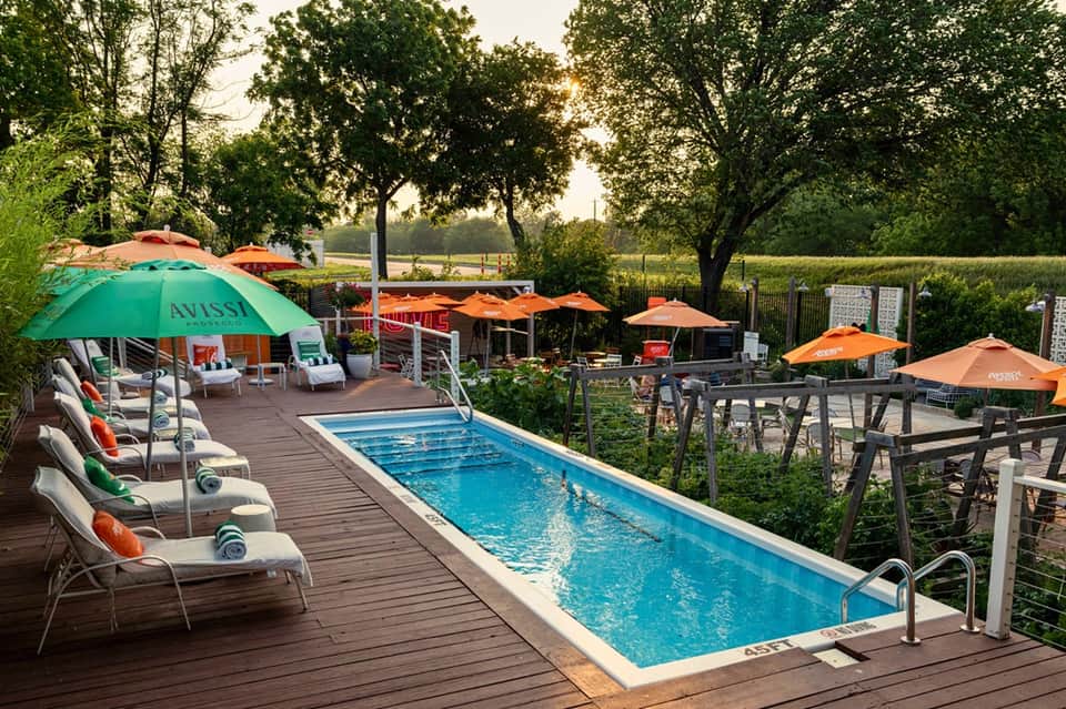 Lap pool with orange umbrellas, lounge chairs, and trees in rural resort setting