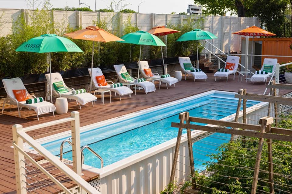 Resort pool deck with white lounge chairs, green and orange umbrellas, and wooden railings