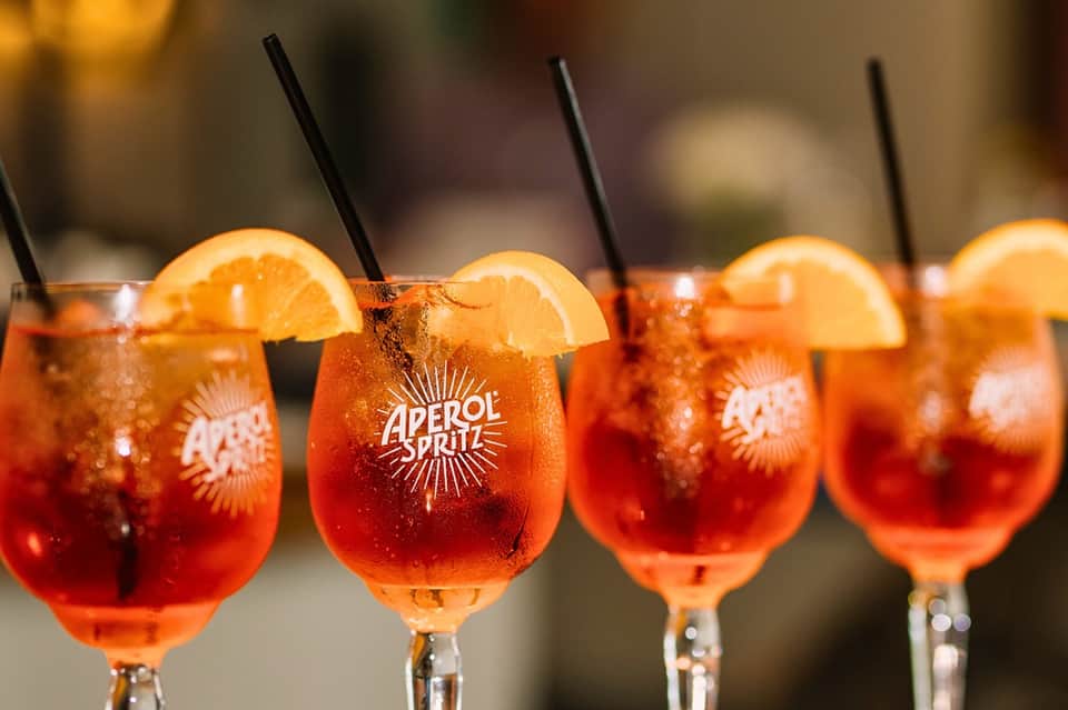 Close-up of Aperol Spritz cocktails with orange slices and black straws on bar counter