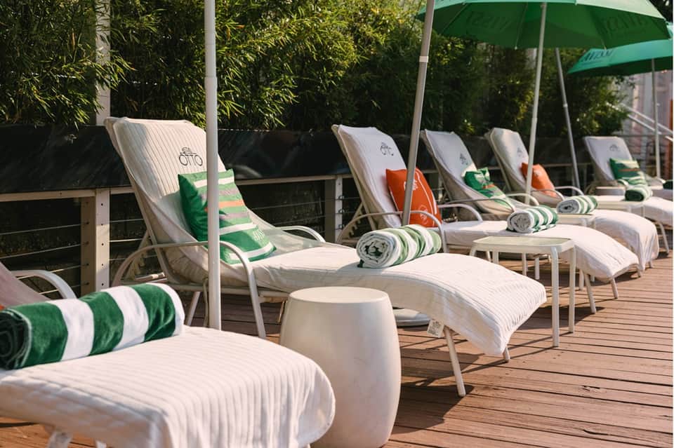 Poolside deck with white striped lounge chairs, green umbrellas, rolled towels, and bamboo privacy screen