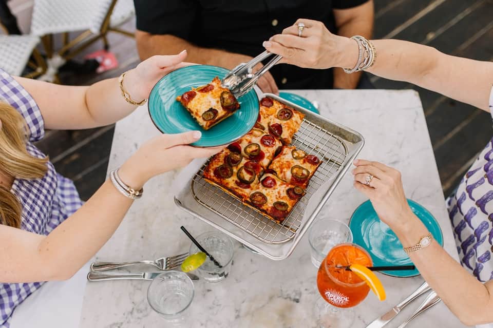 Multiple hands sharing pepperoni pizza from a baking tray at outdoor dining table