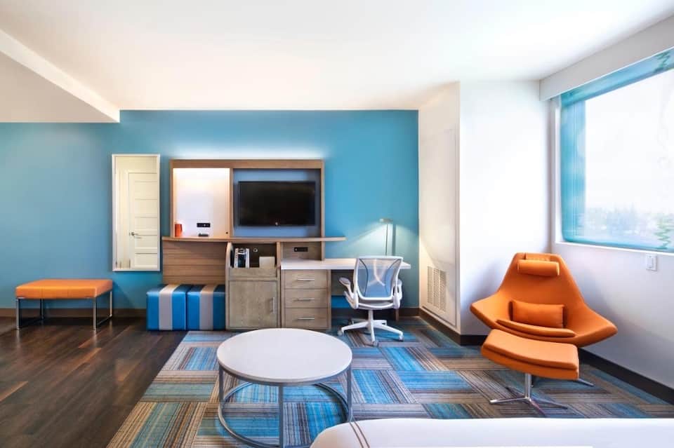 Contemporary hotel room with blue accent wall, orange furniture, and ocean views