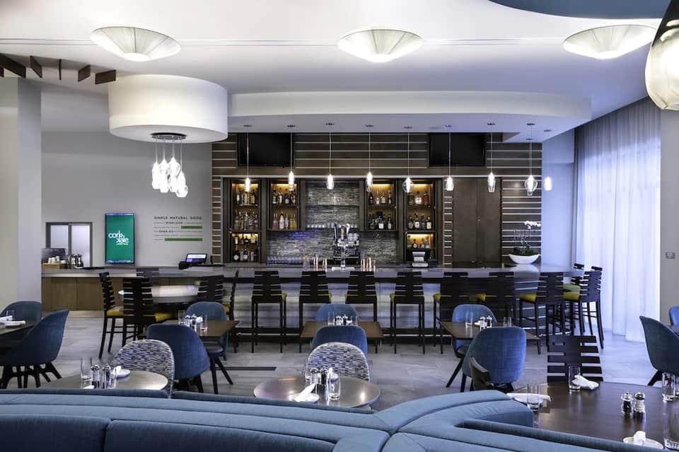 Modern hotel bar and lounge with black seating, pendant lights, and backlit liquor shelves