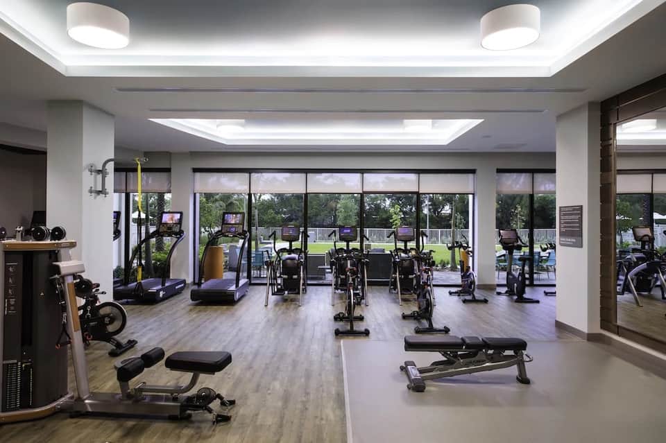 Modern fitness center with cardio equipment, stationary bikes, treadmills, and large windows overlooking grounds
