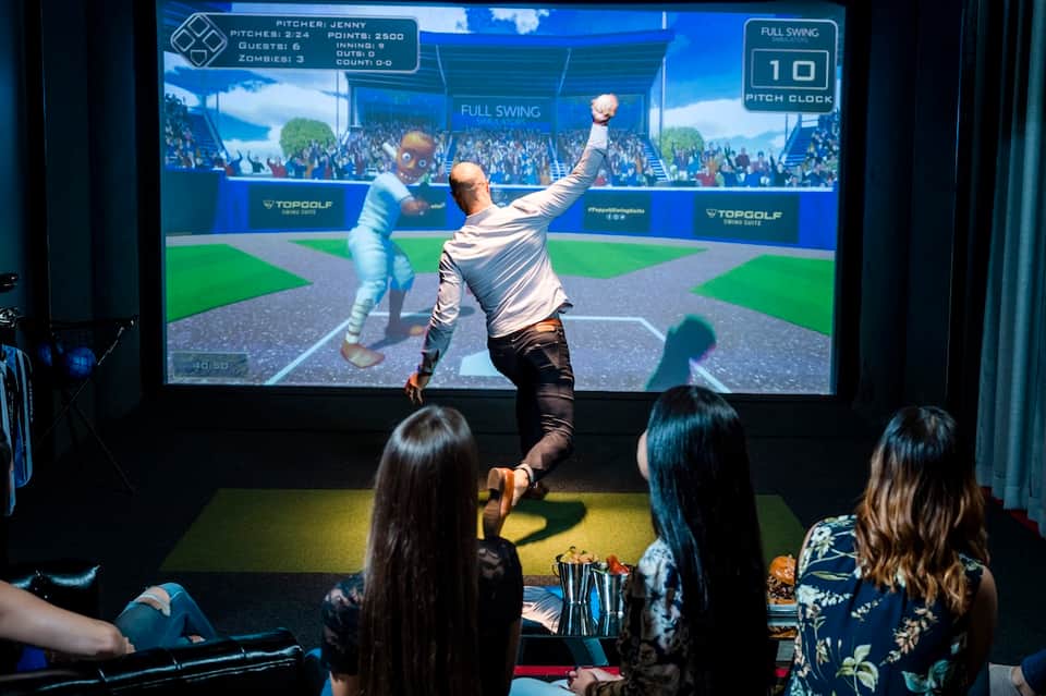 Person playing interactive golf simulation game on large screen at indoor entertainment venue