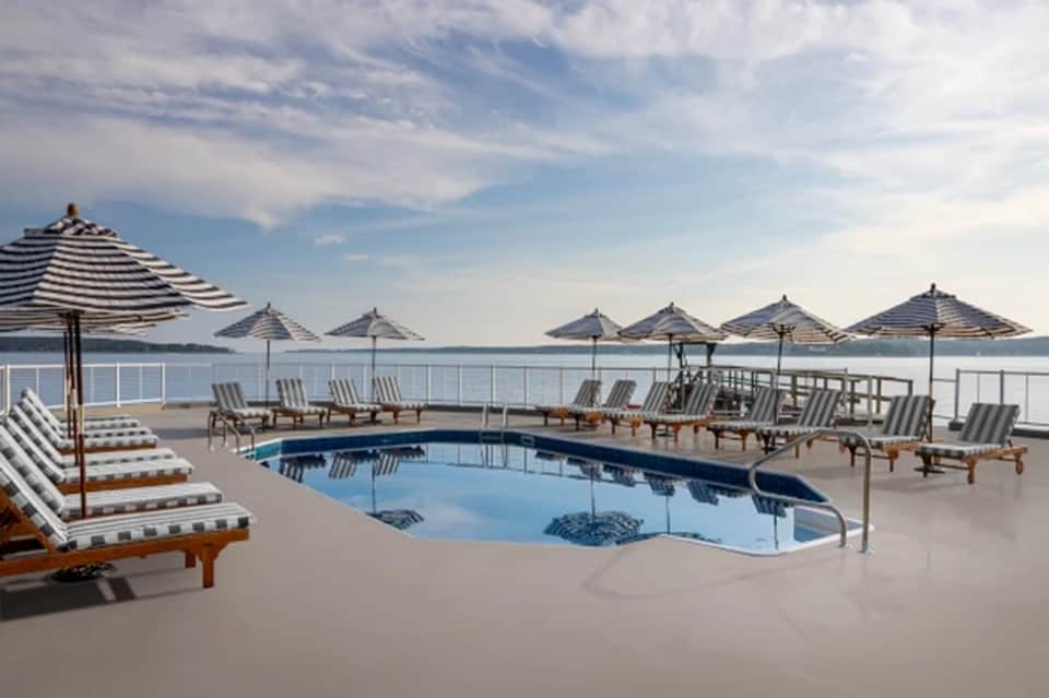 Waterfront pool with striped umbrellas, lounge chairs, and water views at luxury resort