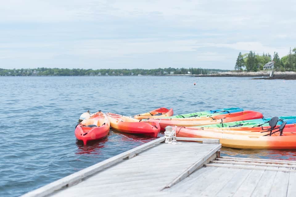Colorful kayaks lined up at a wooden dock on calm blue water with forested shoreline