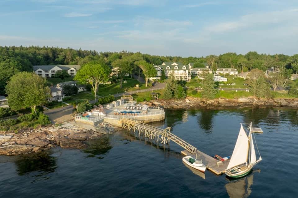 Aerial view of waterfront resort with docked sailboats, beach pavilion, and residential homes