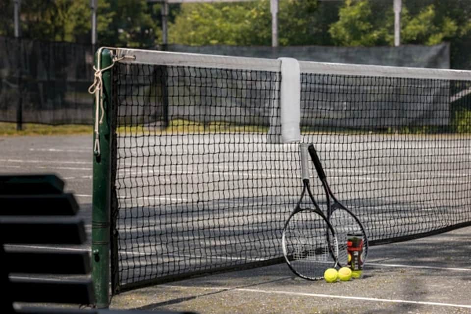 Professional tennis court with net, racket, yellow balls, and sports equipment on concrete surface