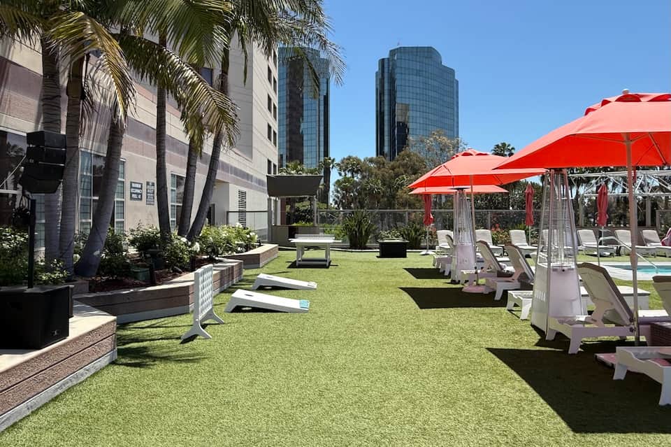 Outdoor lawn area with red umbrellas, white lounge chairs, palm trees, and modern hotel towers