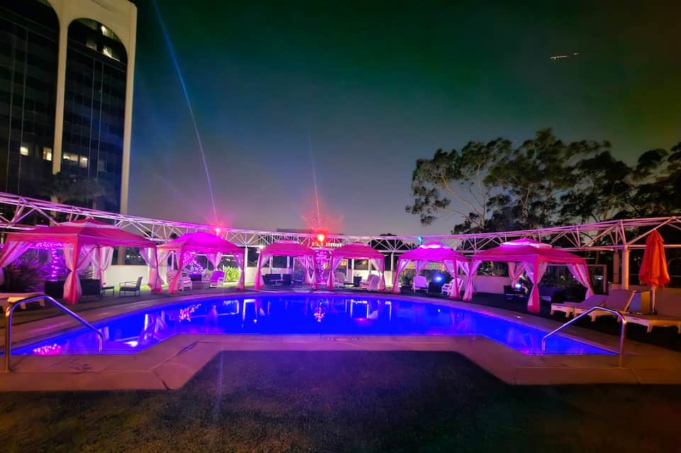 Illuminated resort pool at night with pink and blue LED lighting and covered lounge areas
