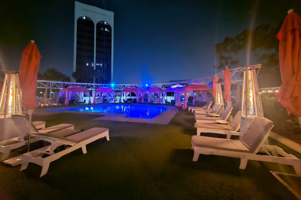 Illuminated resort pool at night with blue lighting, loungers, and heaters