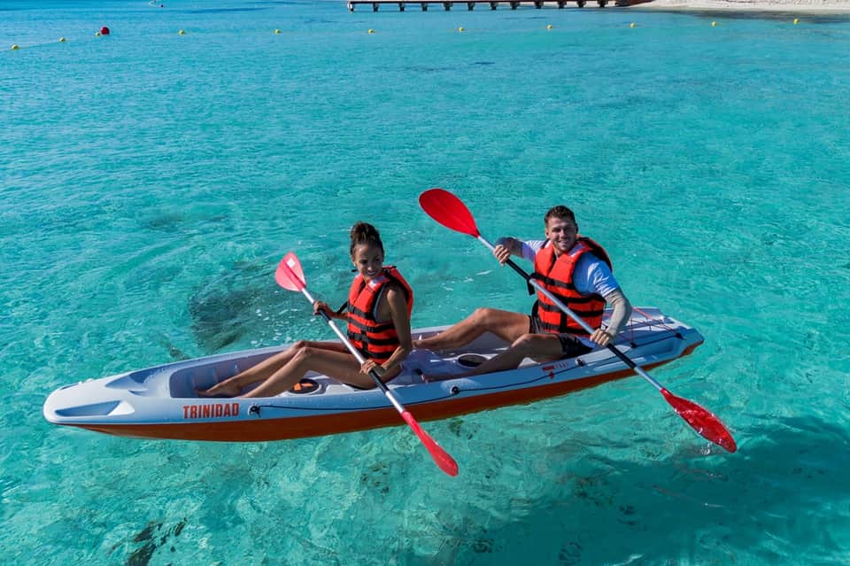 Two people kayaking in crystal clear turquoise water near coastal resort