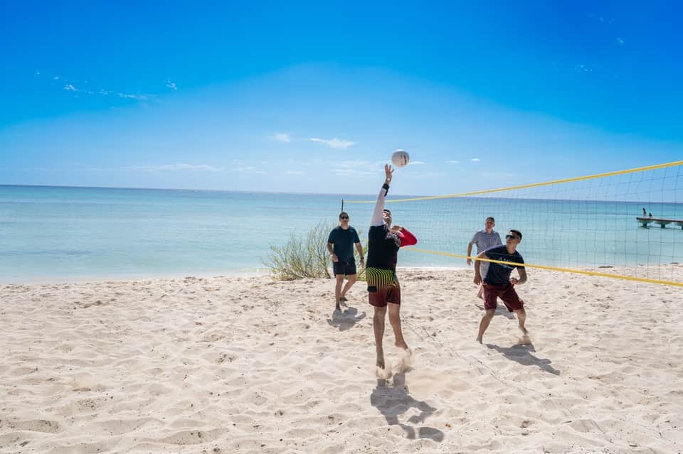 Beach volleyball game with players jumping to hit ball over net under clear blue sky