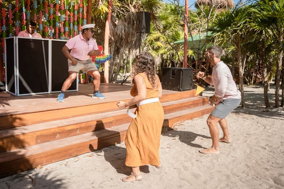 Guests playing cornhole on a beach with palm trees, performance stage, and colorful decorations