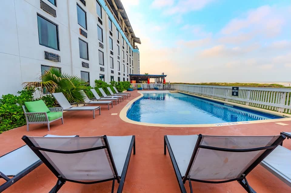 Resort pool with colorful lounge chairs and waterfront views at sunset