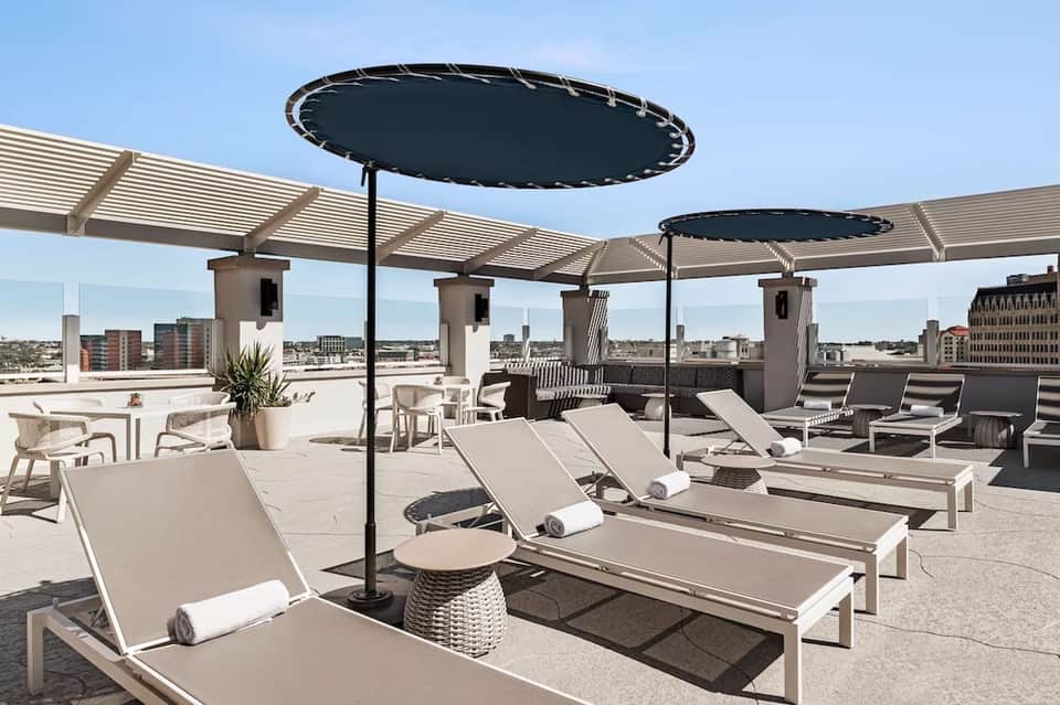 Modern rooftop terrace with lounge chairs, black umbrellas, pergola, and cityscape views in background