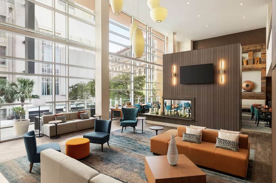 Modern hotel lounge with floor-to-ceiling windows, tan and teal seating, and wood accent wall