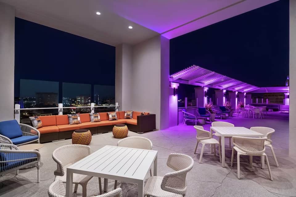 Modern resort terrace with purple ambient lighting, orange seating, and city skyline views