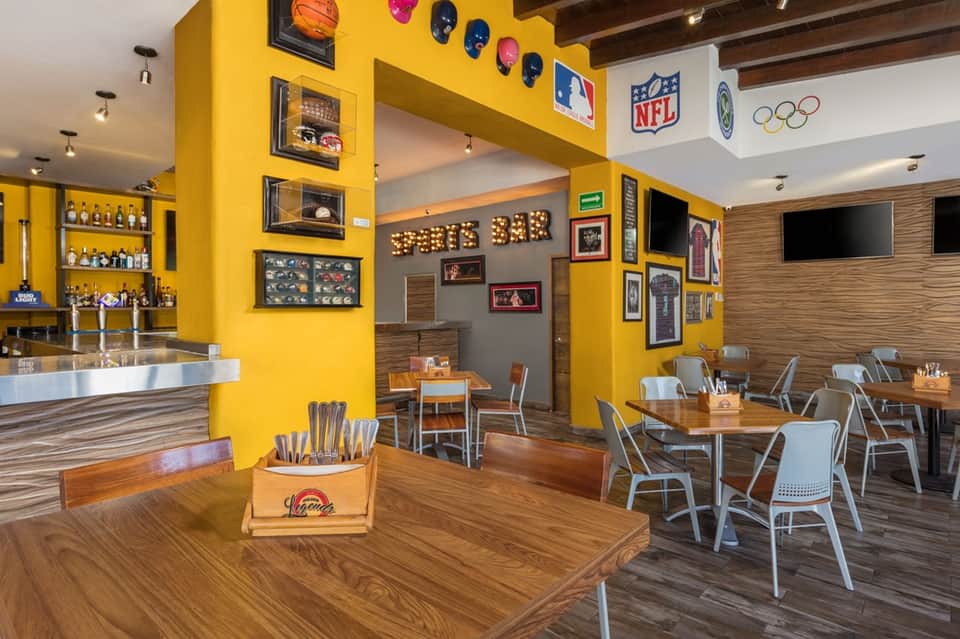 Sports bar interior with bright yellow accent walls, wood flooring, bar counter, and TV screens