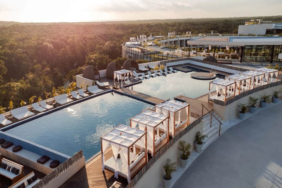 Aerial view of luxury resort pools, loungers, cabanas, and landscaping overlooking forest valley