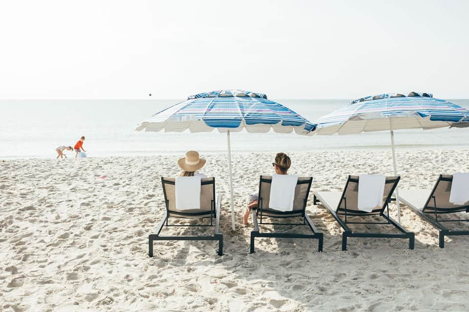Beach lounge area with striped umbrellas, loungers, and ocean view with children playing