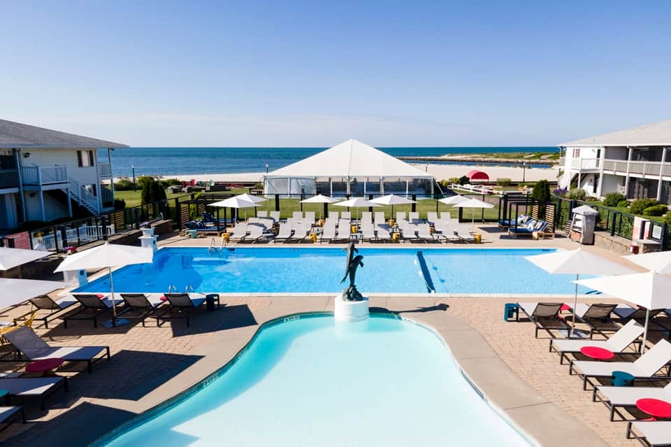 Beachfront resort pool with ocean view, lounge chairs, and white tent pavilion