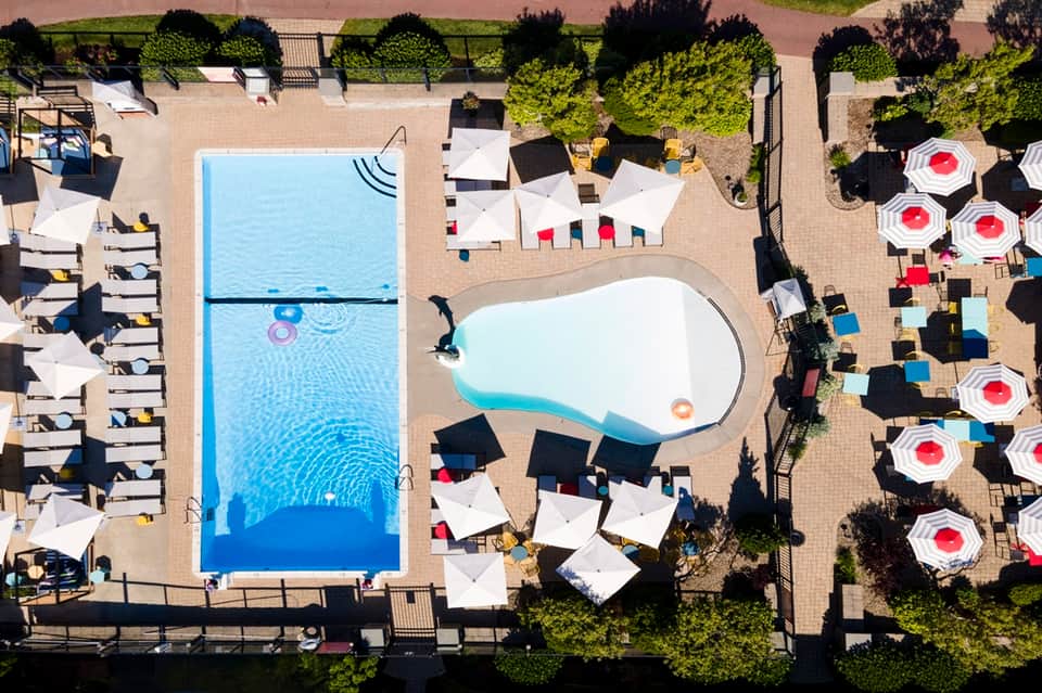Aerial view of resort pool deck with loungers, white umbrellas, and manicured landscaping