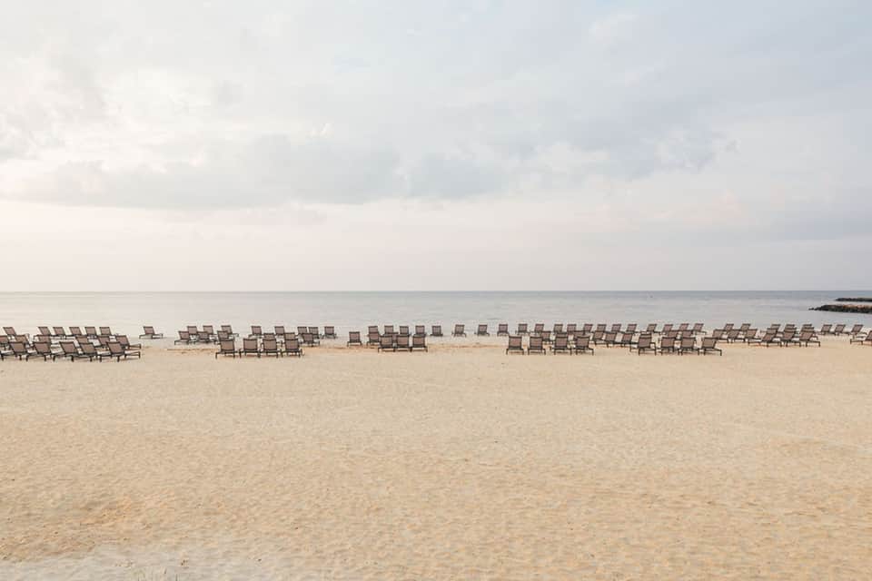Beach scene with rows of empty lounge chairs lined along sandy shore and calm ocean