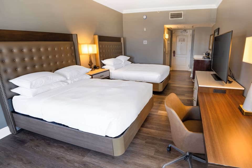 Modern hotel room with two queen beds, tufted headboards, and wooden desk area