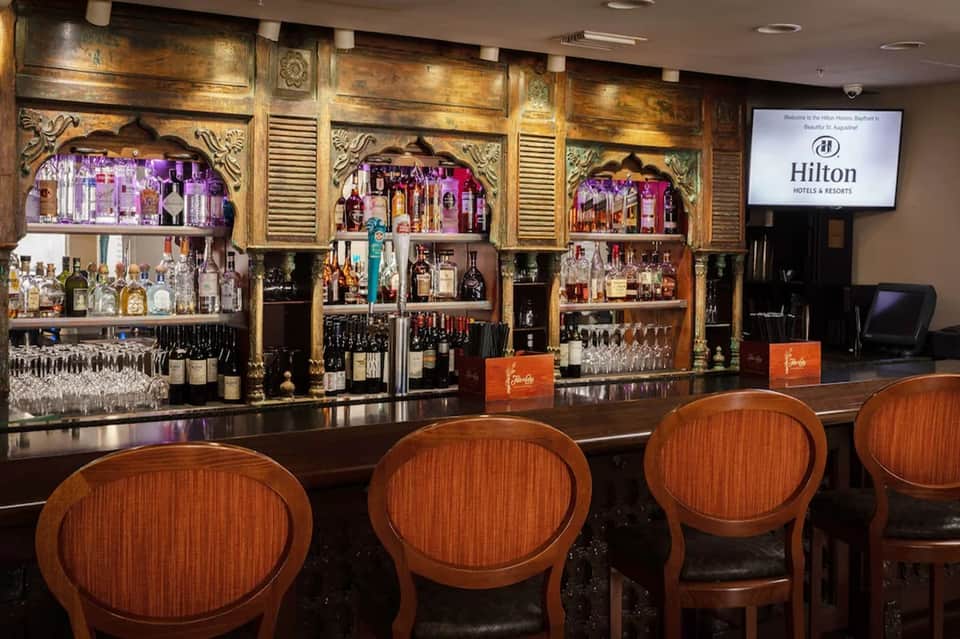 Ornate gold bar interior with decorative shelving, bottles, and wooden bar stools at Hilton hotel