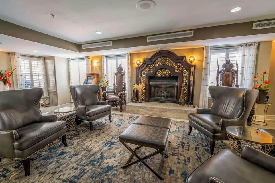 Elegant hotel lounge with fireplace, leather seating, decorative mantel, and tall windows with drapes