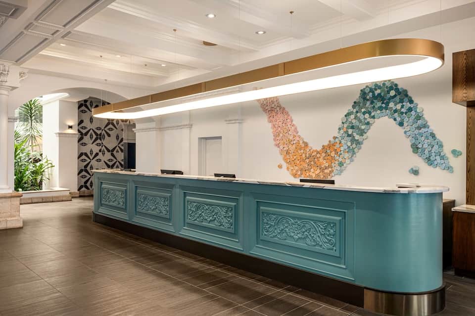 Hotel lobby reception desk with turquoise base and decorative wall art installation