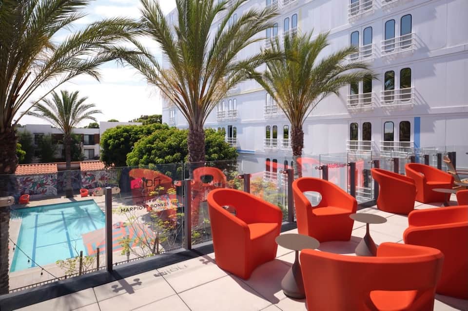 Hotel rooftop lounge with bright red bucket chairs, palm trees, pool area, and ocean views