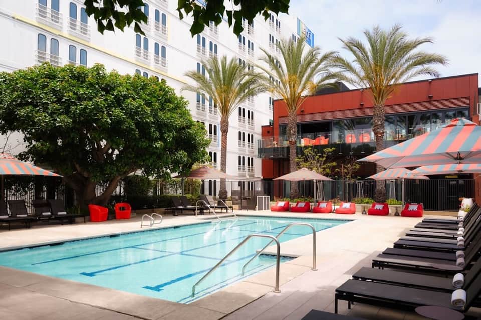 Modern hotel pool with lap lanes, red umbrellas, loungers, and contemporary red-accented building facade