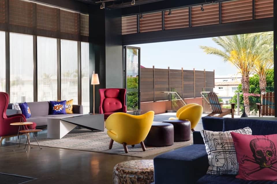 Contemporary lounge with colorful chairs, geometric sofa, large windows, and wooden ceiling accents