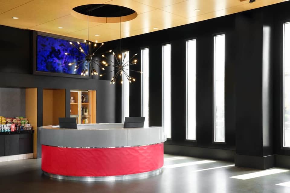 Hotel reception desk with bold red accent wall, black interior, gold ceiling, and contemporary design